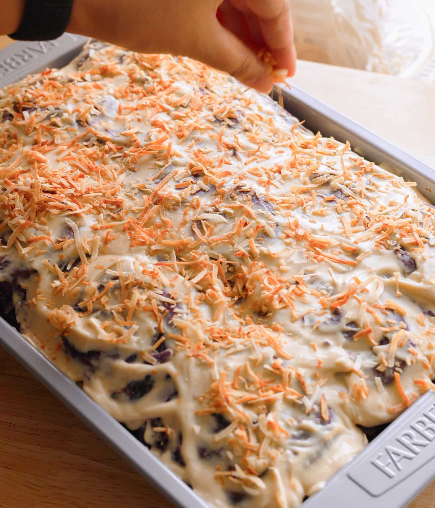 Topping frosted ube brioche coconut rolls with toasted shredded coconut.