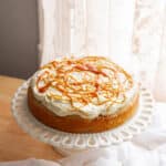 Banana cake topped with banana pudding frosting and caramel, on a cake stand.