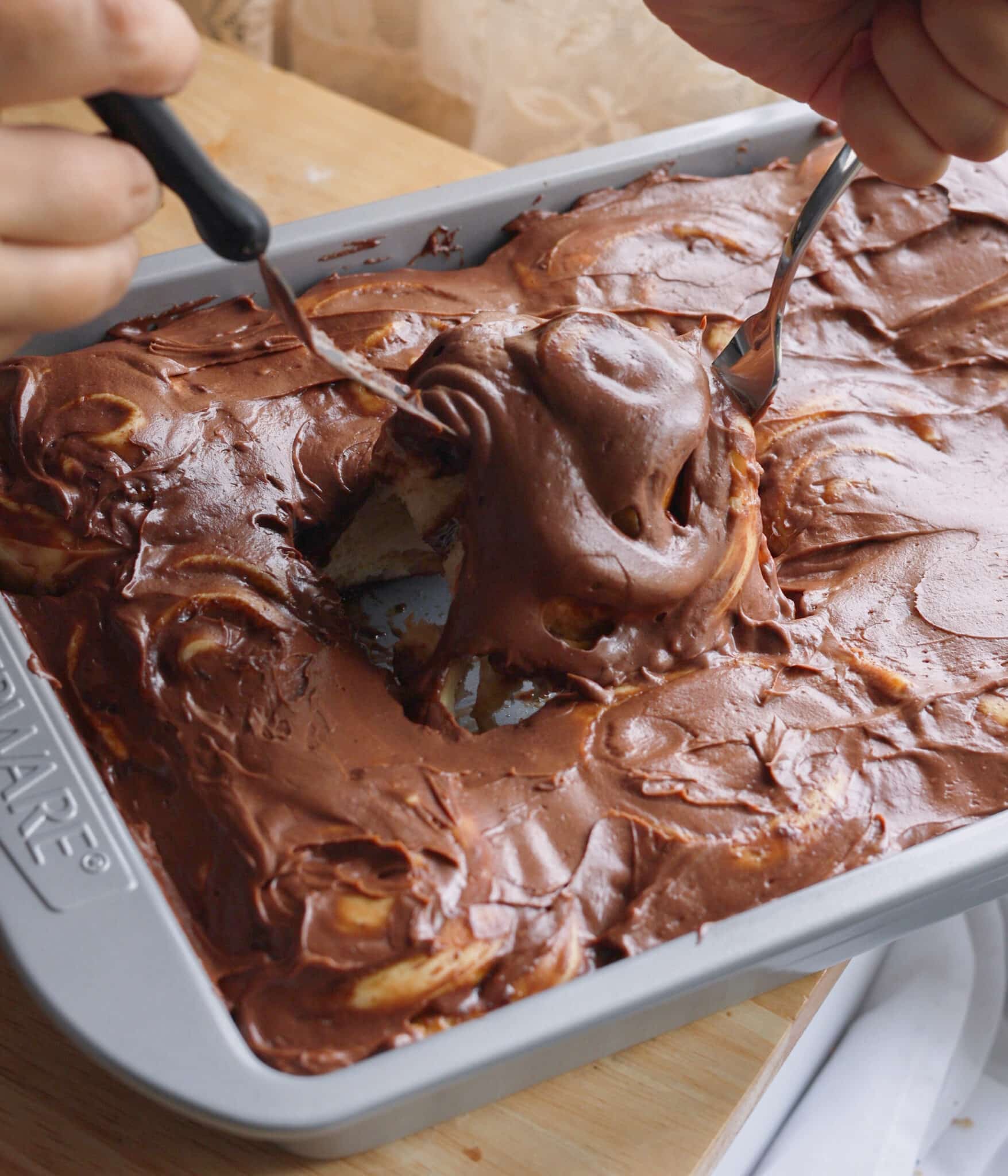Taking chocolate frosted Milo bun out of baking pan.