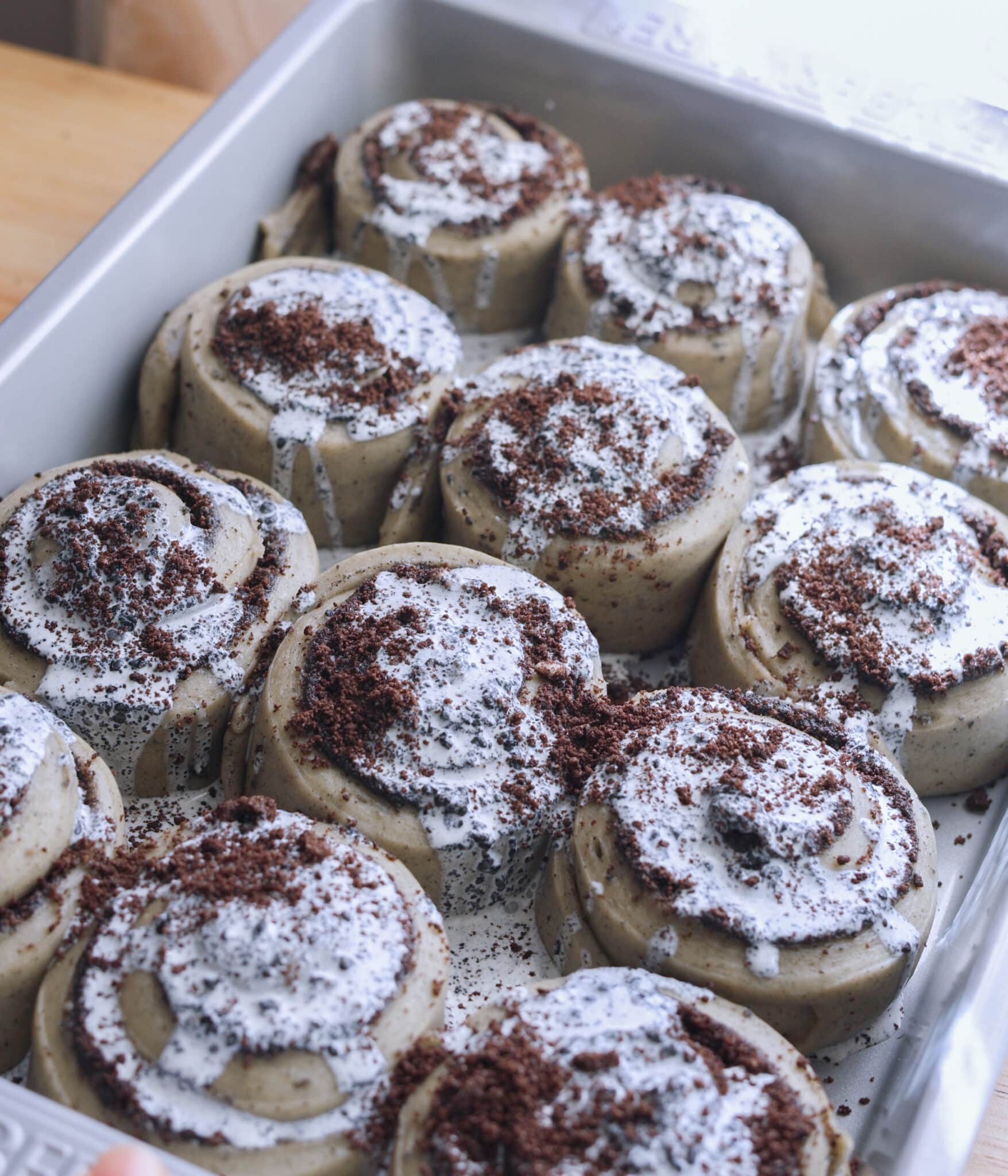 Black sesame heavy cream on top of Oreo black sesame rolls in baking pan.